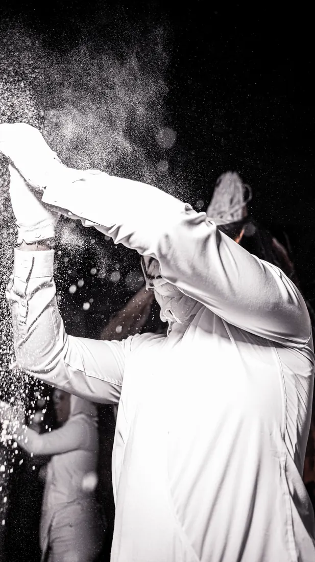 RGR SHOOT, talc projeté au-dessus des costumes blancs pendant un défilé, en noir et blanc