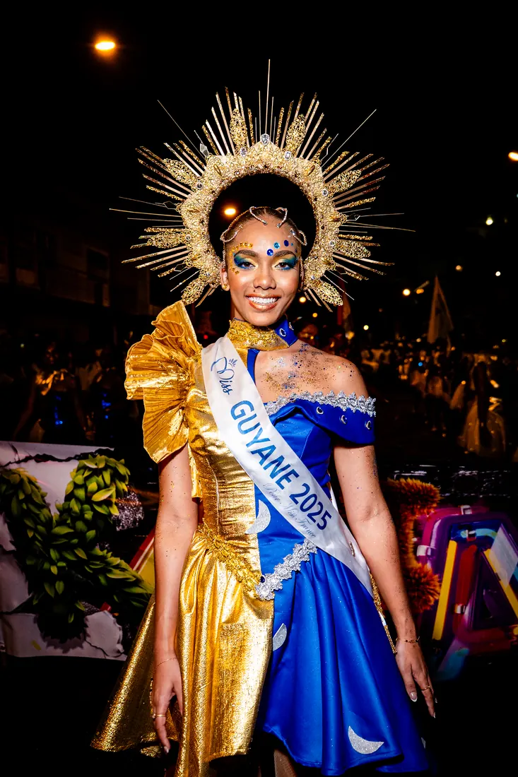 RGR SHOOT, participante en costume doré et bleu, écharpe Guyane 2025, pendant un défilé de nuit